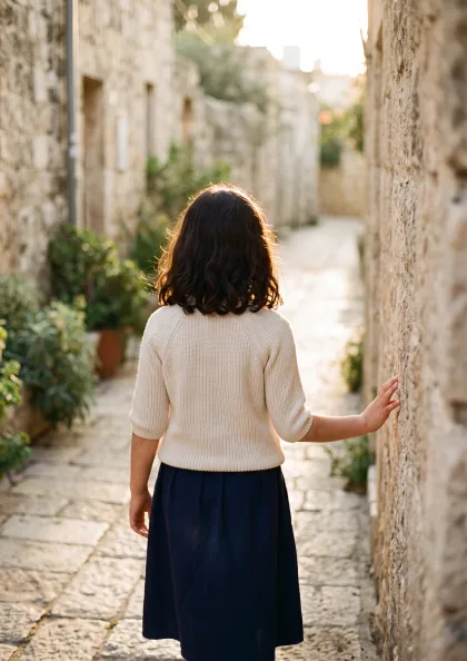 נערה הולכת בשביל אבן בין קירות ישנים באור זהוב