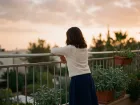 נערה נשענת על מעקה מרפסת בשעת דמדומים, גבה למצלמה