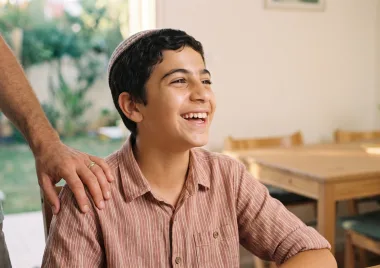 נער צוחק ליד שולחן, יד של מבוגר על כתפו