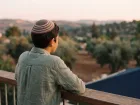 נער נשען על מעקה מרפסת בשעת דמדומים, גבו למצלמה